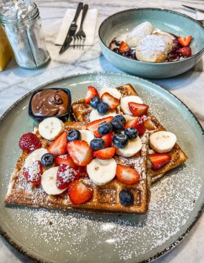 Üstünde taze çilek, ahududu, yaban mersini ve böğürtlen bulunan Belçika Waffle 'larından oluşan lezzetli bir kahvaltı. Akçaağaç şurubuyla kaplanmış ve nane yapraklarıyla süslenmiş..
