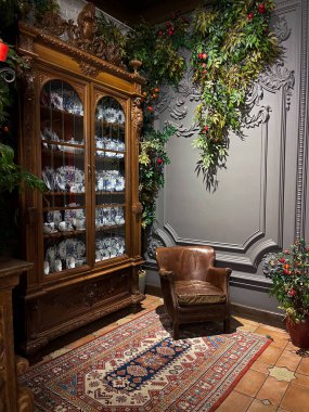 Kahverengi deri koltuğu, antika ahşap porselen dolabı, doğu halısı ve yemyeşil ve meyvelerle süslenmiş klasik duvar pervazı olan zarif bir klasik köşe..