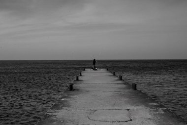 Sırt çantası ve rıhtımda iskelesi olan bir adamın siyah beyaz fotoğrafı.