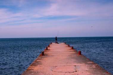Açık gökyüzünün altında bir balıkçı iskelesi olan bir kişinin dikey görüntüsü.