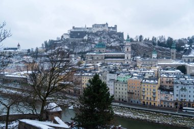 Salzburg 'da kış yürüyüşü, kaldırım taşı sokaklar, büyüleyici eski binalar ve kar ve tarihten oluşan bir battaniyeye sarılmış yüksek kale..