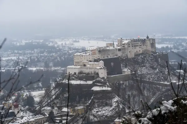Salzburg 'da kış yürüyüşü, kaldırım taşı sokaklar, büyüleyici eski binalar ve kar ve tarihten oluşan bir battaniyeye sarılmış yüksek kale..