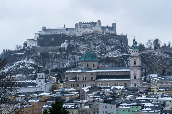 Salzburg 'da kış yürüyüşü, kaldırım taşı sokaklar, büyüleyici eski binalar ve kar ve tarihten oluşan bir battaniyeye sarılmış yüksek kale..