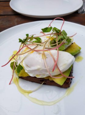 Avokado dilimleri, mükemmel haşlanmış yumurtalar ve taze lahanayla bitirilmiş lezzetli bir zanaatkar tostu. Sunum zarif, zeytinyağı serpiştirilmiş ve özel bir dokunuş eklenmiş..