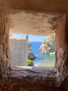 Mavi denizi, engebeli uçurumları ve berrak gökyüzünü kaplayan antik bir kalenin taş oyulmuş bir penceresinden okyanus manzarası, bir tarih ve sükunet duygusu aktarıyor..