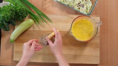 Peynir güzel bir rende rendelenir, bir kadının elleri ahşap bir tahtanın üzerinde, sebzelerin arka planında. Yakın çekim, üst görünüm