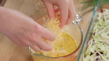 Rendelenmiş peynir yumurta karışımıyla karıştırma kabına dökülüyor. Kızın elleri rendelenmiş peyniri döküyor. Yakın plan.