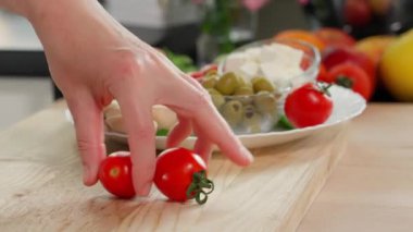 Kızların elleri bir tabak yiyecekten iki küçük kırmızı domates alıyor ve onları tahta bir tahtada dilimlere ayırıyor. Yakın plan, kenar görünüm
