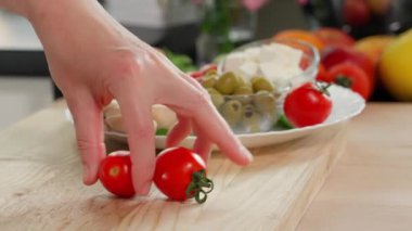 Kızların elleri bir tabak yiyecekten iki küçük kırmızı domates alıyor ve onları tahta bir tahtada dilimlere ayırıyor. Yakın plan, kenar görünüm