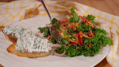 Kızın eli salatayı çatalla deliyor ve gösteriyor. Salata bruschetta ile birlikte yuvarlak bir tabakta yatıyor. Yakın plan..