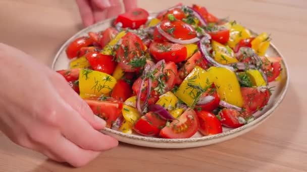 少女の手がサラダの皿を紡いでいる 赤トマト 黄色唐辛子 玉ねぎ ハーブで完成したサラダのデモンストレーション クローズアップ — ストック動画