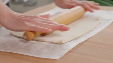 Dişi eller, tahta bir masanın üzerinde tahta bir raptiyeyle dikdörtgen puf böreği serer. Yan görünüm, yakın plan