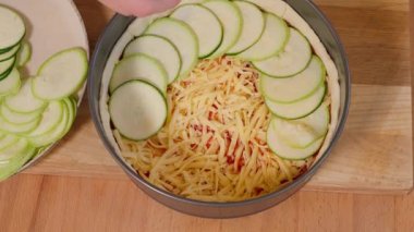 Domates soslu ev yapımı pasta ve ahşap bir masada fırın kabında peynir. Kızın elleri hamurlu turtaya kabak dilimleri koyar. Organik turta. Üst görünüm, yakın çekim