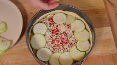 Ahşap bir masadaki fırın kabını dolduran ev yapımı pasta. Kızlar kabak dilimlerini peynirli hamur turtasına koyuyorlar. Organik turta. Üst görünüm, yakın çekim