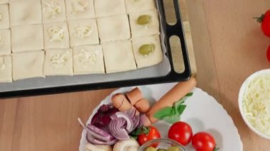 Bayram için atıştırmalık hazırlıyorum. Kare aperatifler ahşap bir masadaki fırın kabında puf böreğinden yapılmış, kızın elleri feta peyniri seriyor. Üst görünüm, yakın çekim