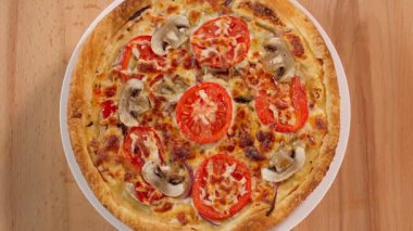 Mantarlı, peynirli ve domatesli taze pişmiş pizza. Pizza ahşap bir masanın üstünde daire şeklinde dönüyor, yakın plan, üst manzara.