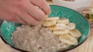 Bir kadın sağlıklı vegan besleyici bir kahvaltı hazırlar, yulaf ezmesi, muz ve kuru üzümleri yulaf ezmesi ve ahşap bir tabağa koyar. Sağlıklı kahvaltı, diyet konsepti. Yakın plan.