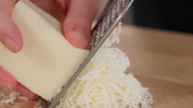 Mozzarella peyniri ahşap bir masada ince bir rende kullanılarak rendelenir. Yakın plan.