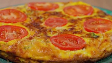 Sağlıklı vejetaryen yemekleri. Domatesli omlet, yuvarlak tabakta dönen frittata, ahşap masa. Yakın plan, kenar görünüm.