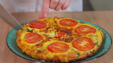 Domatesli omlet, kabak, peynir ve otlar, yuvarlak tabakta frittata, dilimler halinde ahşap bir masada. Sağlıklı vejetaryen yemekleri. Yakın çekim, üst görünüm.