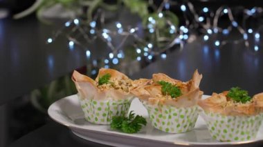 Oval tabağı dolduran taze filo pasta aperatifleri, siyah yüzey, soldan sağa hareket eden kamera. Tatil için yemek, açık büfe aperatifleri. Çeşitli fırınlanmış yiyecekler. Macro, önden bak.