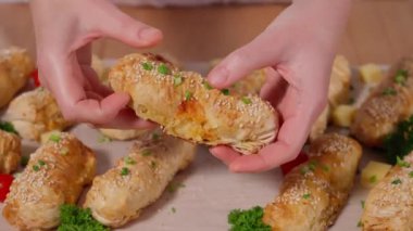 Kızın elleri ahşap bir tahtanın yarısını doldurarak taze pişmiş fileto hamurlu turtayı kırıyor. Çeşitli fırınlanmış yiyecekler. Susamlı hamurdan yapılan tereyağlı hamur işleri. Puf böreği. Macro, önden bak.