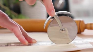 Şef hamuru pizza bıçağıyla şeritler halinde keser, kamera bıçakla hareket eder. Hamur hazırlığı, hamurdan peynir çubukları, puf böreği aperatifleri. Yakın plan, kenar görünüm