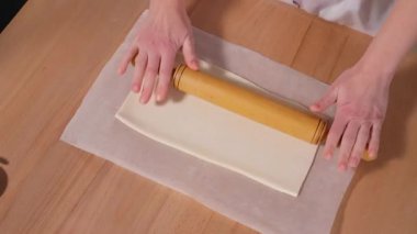 Şef ahşap bir masada merdaneyle hamuru yuvarlıyor. Hamur hazırlığı, dolgulu güzel kokulu turta, puf böreği. Yakın çekim, üst görünüm