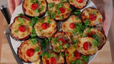 Şef, domates soslu, peynirli, domatesli, ahşap masadaki doldurulmuş patlıcanları gösteriyor. Sağlıklı yiyecekler, sebzeler, patlıcan tabakları, fırında patlıcan, atıştırmalık. Makro, üst görünüm