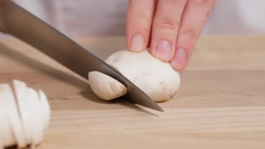 Yakından bakınca, şef şampiyon mantarlarını tahta bir tahtada dilimlemek için keskin bir bıçak kullanıyor. Salatalar için hazırlık, mantarlı mini pizza, turta, aperatif. Yakın plan, ön görünüm