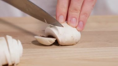 Yakından bakınca, şef şampiyon mantarlarını tahta bir tahtada dilimlemek için keskin bir bıçak kullanıyor. Salatalar için hazırlık, mantarlı mini pizza, turta, aperatif. Yakın çekim, ön görüntü, yavaş çekim