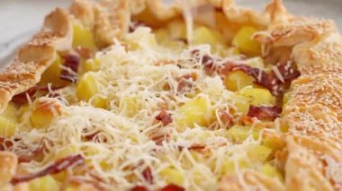 Peynir, patatesli ve pastırmalı sıcak bir turtada rendelenmiş, susam tohumları serpiştirilmiş, yakın plan. Patates tabakları, haşlanmış patatesler, turta ve atıştırmalıklar. Yakın plan, kenar görünüm