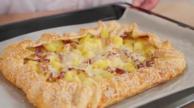 Fırında pişmiş patates ve pastırmalı turta üzerine susam tohumları serpiştirilmiş bir tepsi, daire şeklinde düzgün kamera hareketi. Patates tabakları, haşlanmış patatesler, turta ve atıştırmalıklar. Yakın plan, kenar görünüm