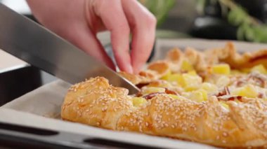 Taze pişmiş patates ve pastırmalı turta, susam tohumları serpiştirilmiş, bir parça turta pişirme tepsisinde kesiliyor. Patates tabakları, haşlanmış patatesler, turta ve atıştırmalıklar. Yakın plan, kenar görünüm