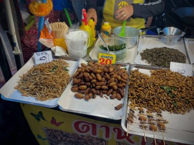 Tayland, Phuket, 11 Aralık 2024 - Bir kadın çeşitli larva türlerinin yanı sıra akrep ve cırcır böcekleri satar. Asya egzotik yemekleri.