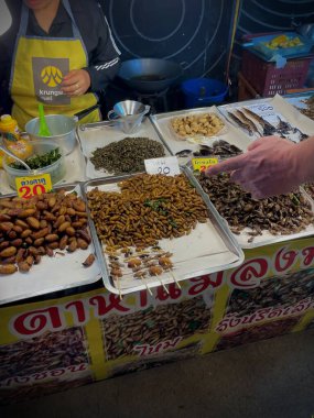 Tayland, Phuket, 11 Aralık 2024 - Bir kadın çeşitli larva türlerinin yanı sıra akrep ve cırcır böcekleri satar. Asya egzotik yemekleri.
