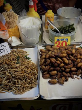 Tayland, Phuket, 11 Aralık 2024 - Bir kadın çeşitli larva türlerinin yanı sıra akrep ve cırcır böcekleri satar. Asya egzotik yemekleri.