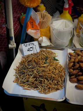 Tayland, Phuket, 11 Aralık 2024 - Bir kadın çeşitli larva türlerinin yanı sıra akrep ve cırcır böcekleri satar. Asya egzotik yemekleri.