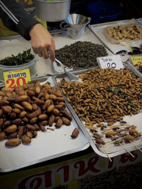 Tayland, Phuket, 11 Aralık 2024 - Bir kadın çeşitli larva türlerinin yanı sıra akrep ve cırcır böcekleri satar. Asya egzotik yemekleri.