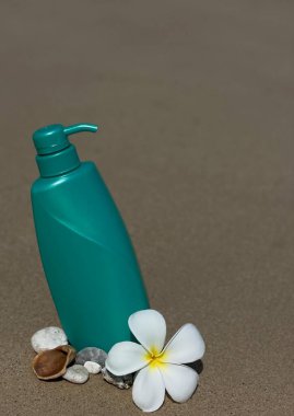 Frengipani çiçeklerinin, deniz kabuklarının ve kumdaki taşların arasına konmuş turkuaz bir şişe. Doğal kozmetik ürünleri, vücut bakımı, SPA, yaz, doğa ve eko-stil.