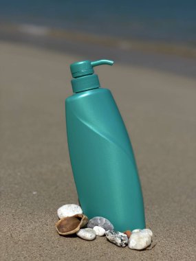 Frengipani çiçeklerinin, deniz kabuklarının ve kumdaki taşların arasına konmuş turkuaz bir şişe. Doğal kozmetik ürünleri, vücut bakımı, SPA, yaz, doğa ve eko-stil.