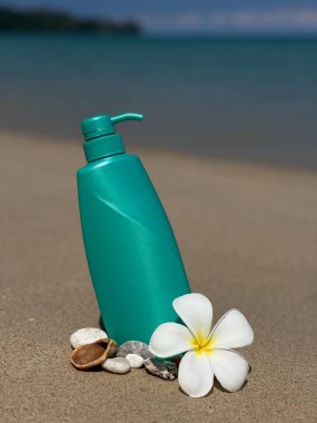 Frengipani çiçeklerinin, deniz kabuklarının ve kumdaki taşların arasına konmuş turkuaz bir şişe. Doğal kozmetik ürünleri, vücut bakımı, SPA, yaz, doğa ve eko-stil.