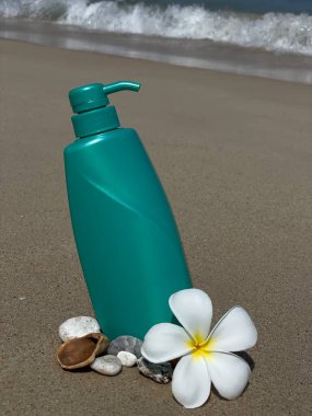 Frengipani çiçeklerinin, deniz kabuklarının ve kumdaki taşların arasına konmuş turkuaz bir şişe. Doğal kozmetik ürünleri, vücut bakımı, SPA, yaz, doğa ve eko-stil.