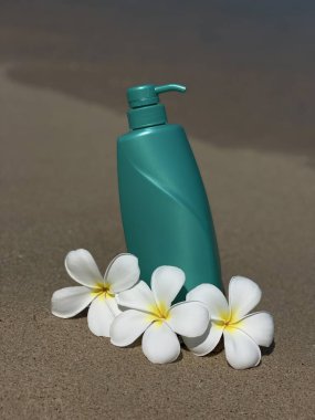 Frengipani çiçeklerinin, deniz kabuklarının ve kumdaki taşların arasına konmuş turkuaz bir şişe. Doğal kozmetik ürünleri, vücut bakımı, SPA, yaz, doğa ve eko-stil.