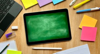 Ahşap bir masada, okul yönetimini taklit eden yeşil bir geçmişi olan bir tablet var. Okul malzemeleri etrafa saçılmış. Okul için hazırlanılıyor.