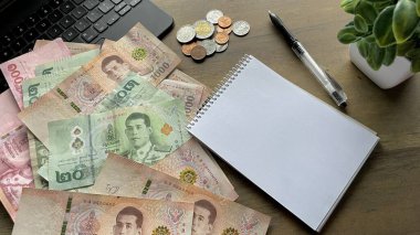 Tayland banknotları ve paraları ahşap masa, yakınındaki defter ve kalem - Tayland 'da mali planlama, harcamalar ve bütçe kavramı.