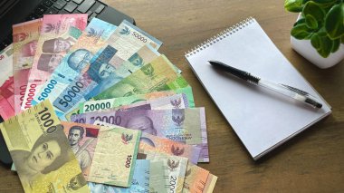 Masanın üzerinde bir rkchka ve Endonezya rupiası (para) bulunan bir defter var. Bütçe, ekonomi, muhasebe, finans, hesaplamalar ve Endonezya para birimi konularına uygundur.