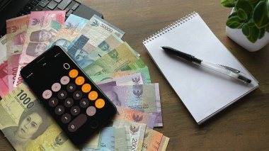 Masanın üzerinde bir rkchka ve yanında da bir hesap makinesinin altında farklı mezheplerden oluşan Endonezya rupiası (para) bulunur. Endonezya bütçe, ekonomi, muhasebe, finans, hesaplamalar ve para biriminde değişiklik.