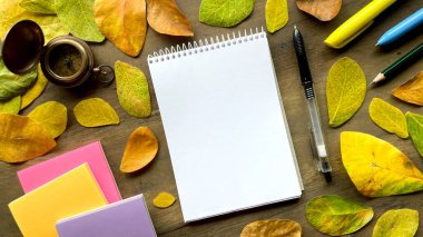 Renkli yapraklar ve kırtasiye ile çevrili boş not defteri ile düz kompozisyon - yaratıcılık, yazma veya planlama için ilham.