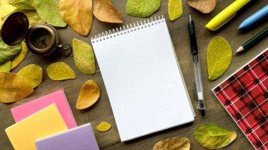 Kırtasiyeli sonbahar kompozisyonu - not defteri, kalem ve defterler sarı ve turuncu yapraklara karşı. Okul konseptine geri dönmek ya da sonbaharda okula gitmek..